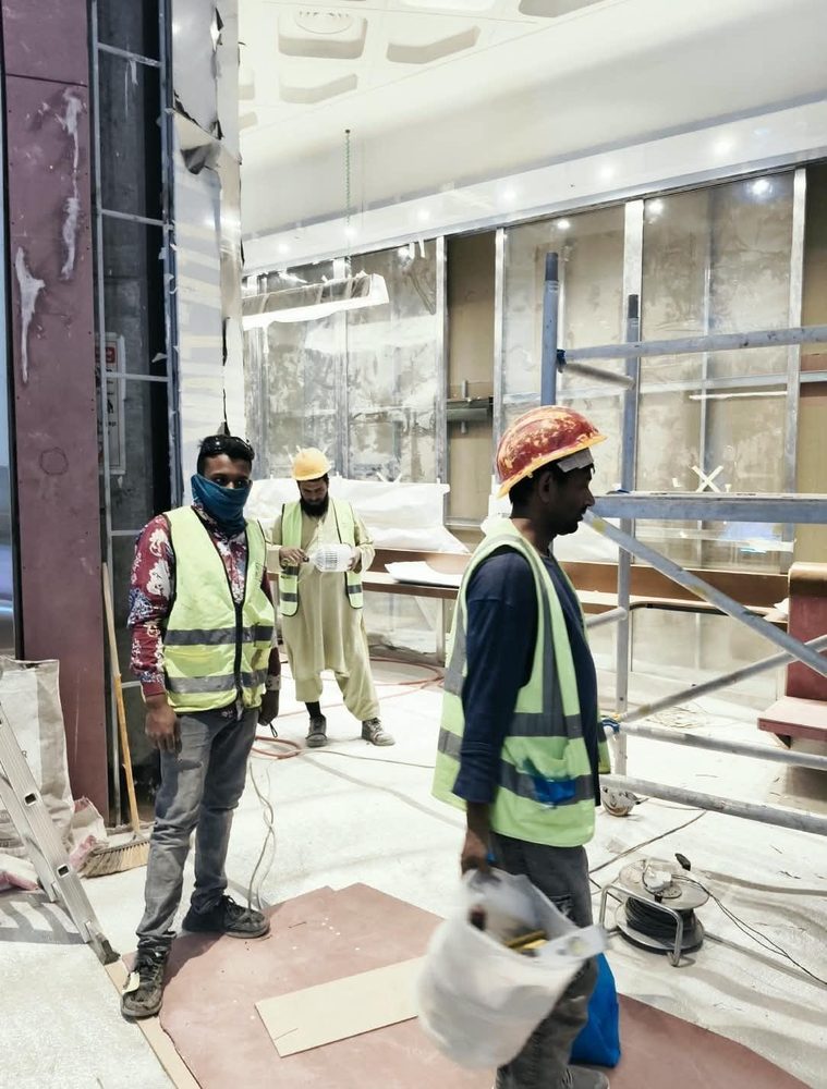 Three technicians in high-visibility vests on a commercial fit-out, with a suspended ceiling and lighting overhead